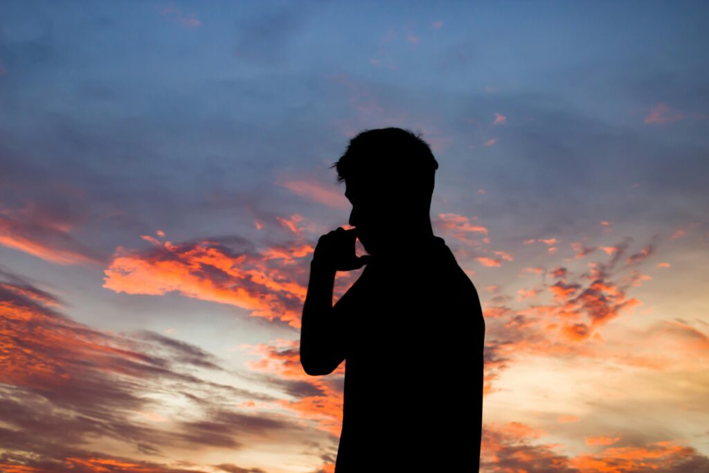 A striking silhouette of a man contemplating under a colorful sunset sky, evoking a sense of tranquility.