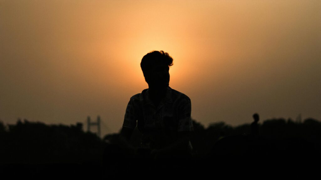 Silhouette of a person under a stunning orange sunset with cityscape in the background.