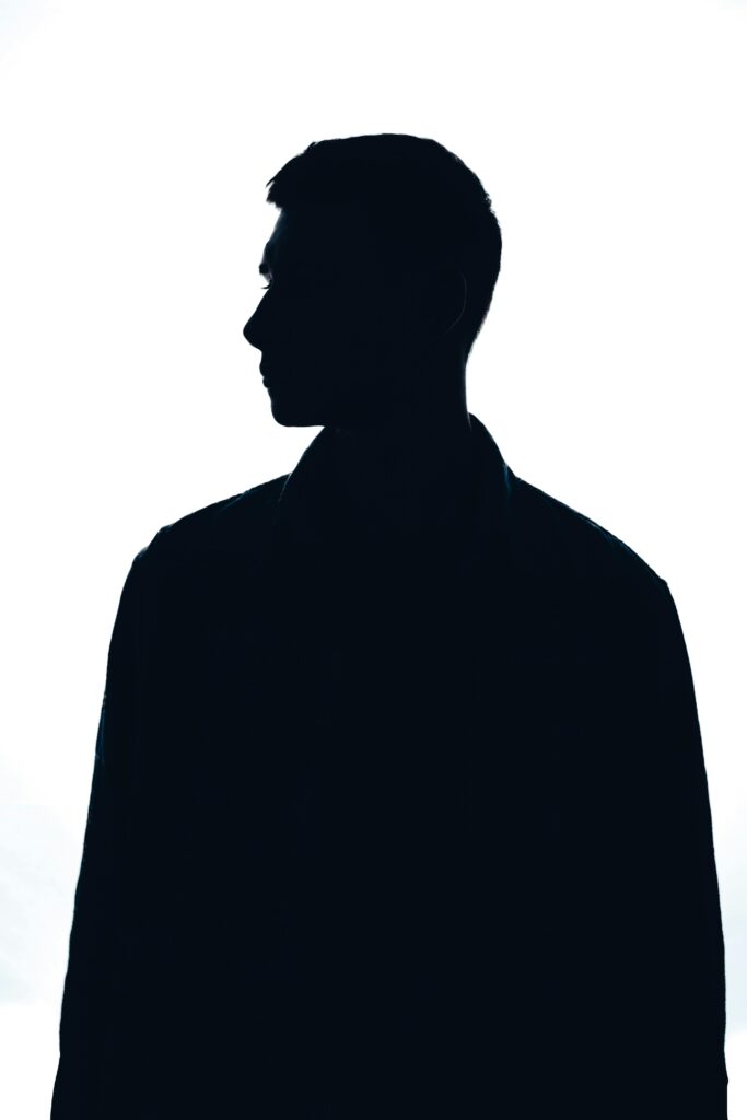 Silhouette of a man in profile view against a bright white background, creating a moody atmosphere.