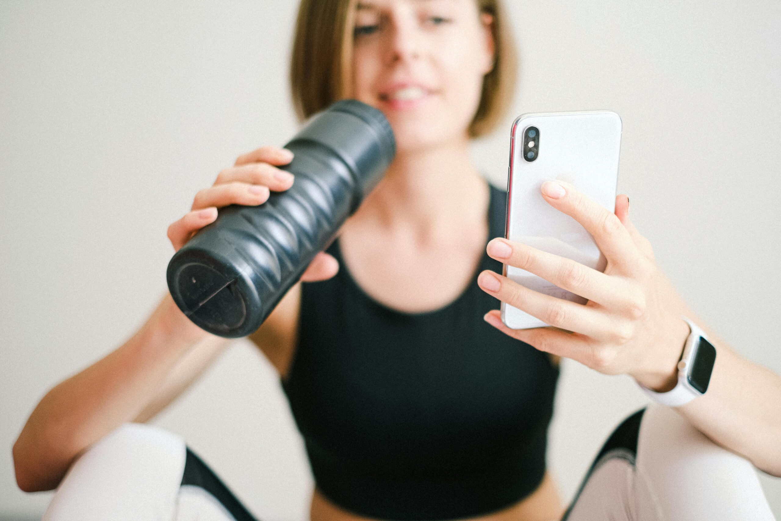 Woman checks smartphone while hydrating with sports bottle during a home workout.
