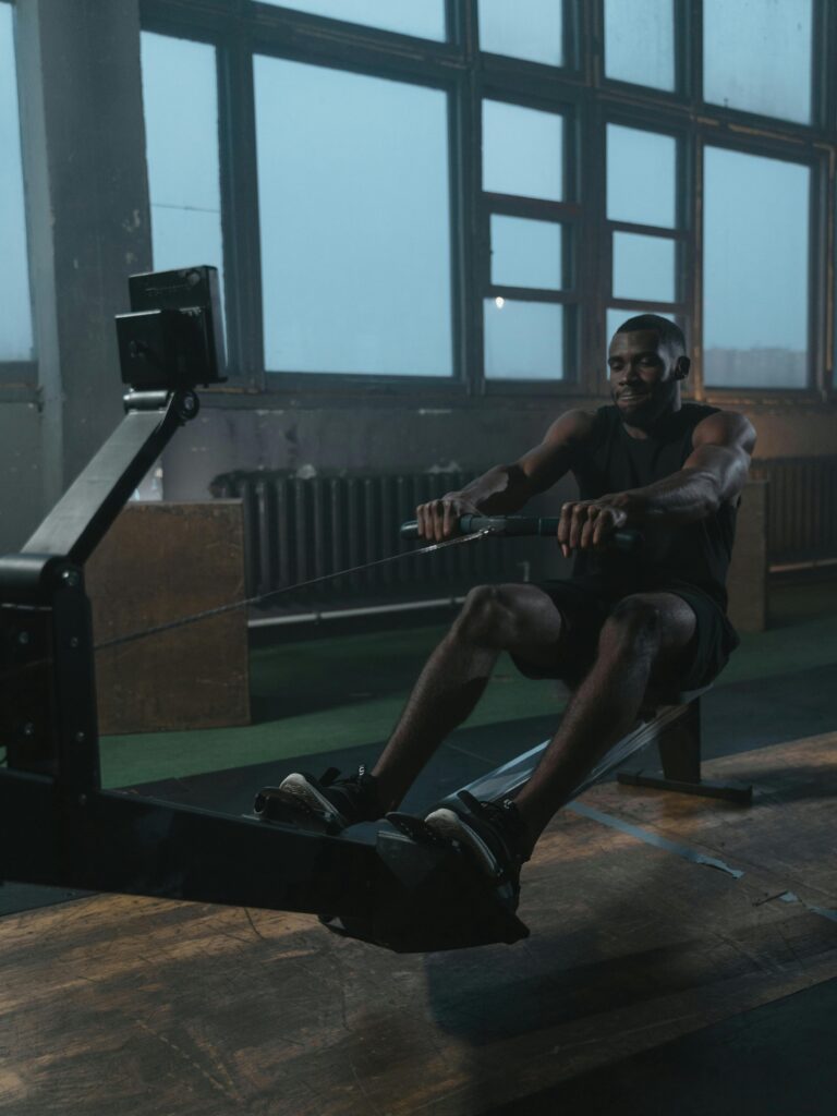 Adult black man intensely working out on a rowing machine indoors. Fitness and strength training concept.